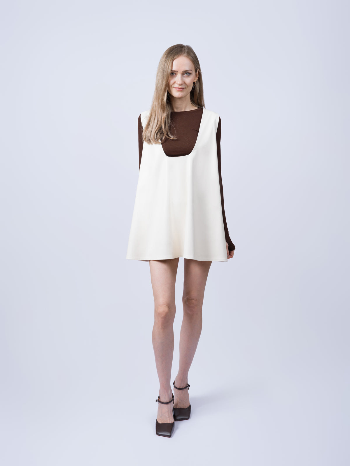 Women’s ecru vegan leather pinafore dress shown from an angled view. Featuring a relaxed oversized silhouette, clean lines and contemporary layering design.