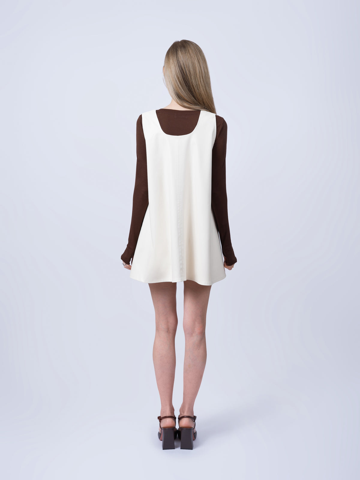 Women’s ecru vegan leather pinafore dress shown from the back. Highlighting the relaxed oversized silhouette, sleeveless construction and timeless contemporary design.